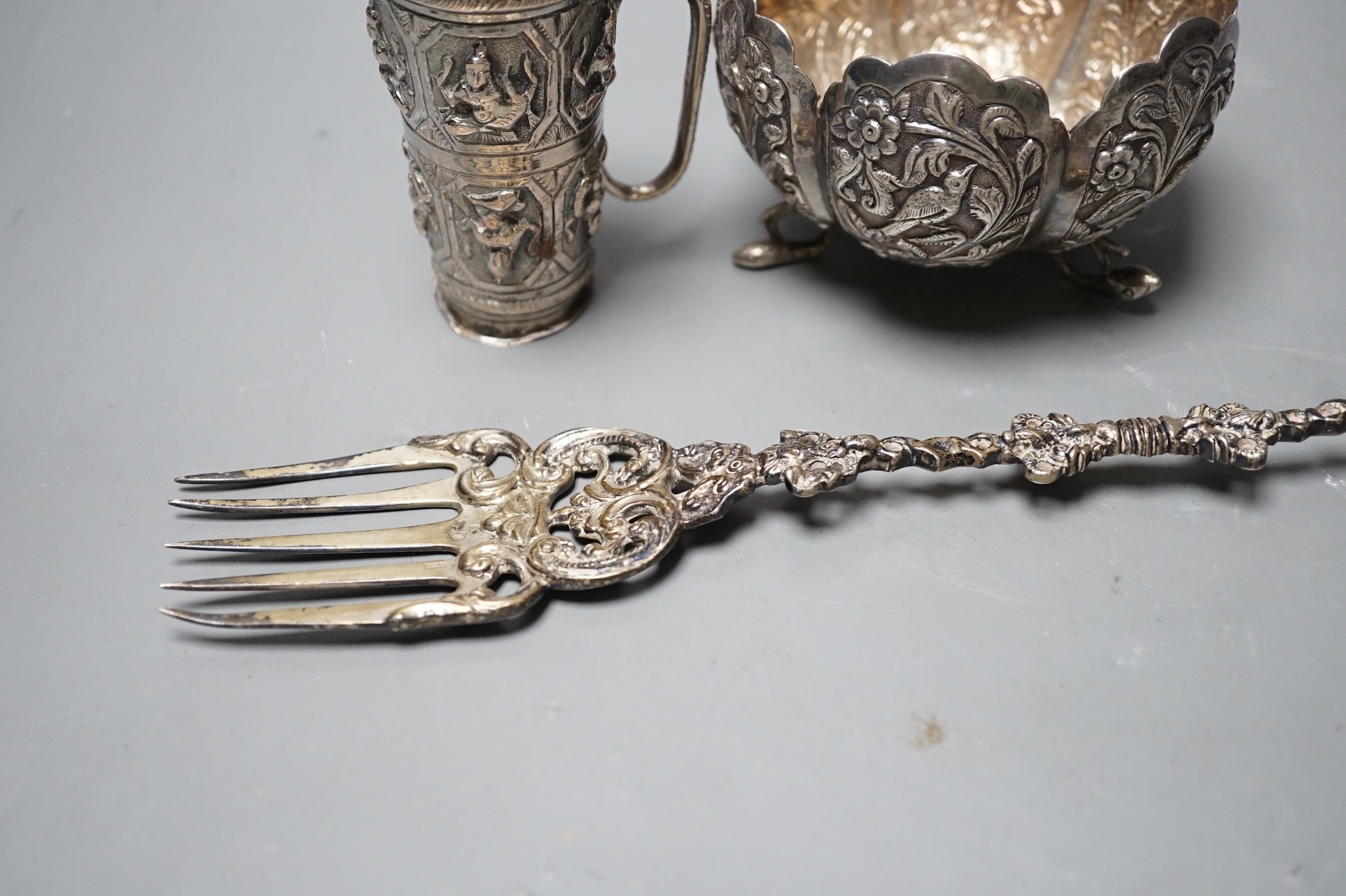 A Dutch white metal toasting fork, with pepperette? finial modelled as a bird, 28.5cm, an Indian white metal double measure cup and a similar bowl.